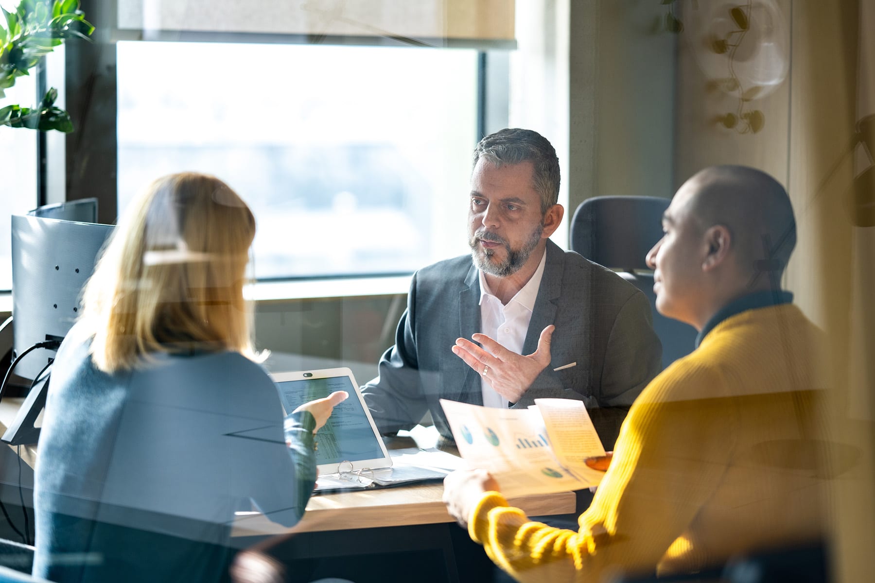 3 individuals sitting at a table discussing and looking at a laptop