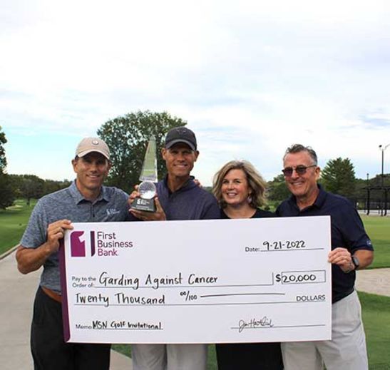 Four individuals on a golf course holding a large check for $20,000 for Garding Against Cancer