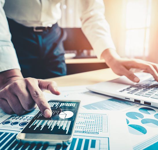 a hand on a phone and computer with charts