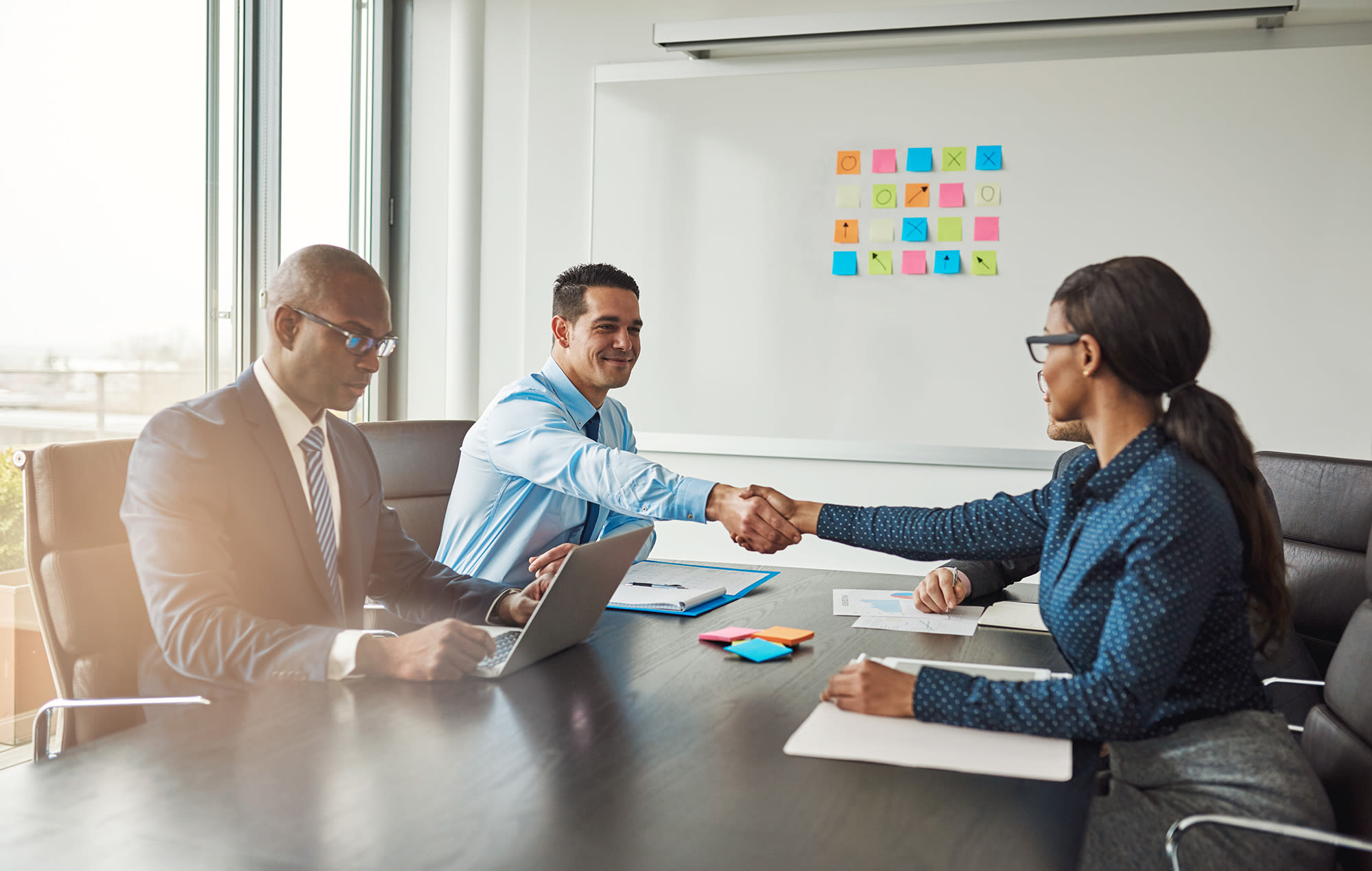 three people meeting around a table and two of them are shaking hands