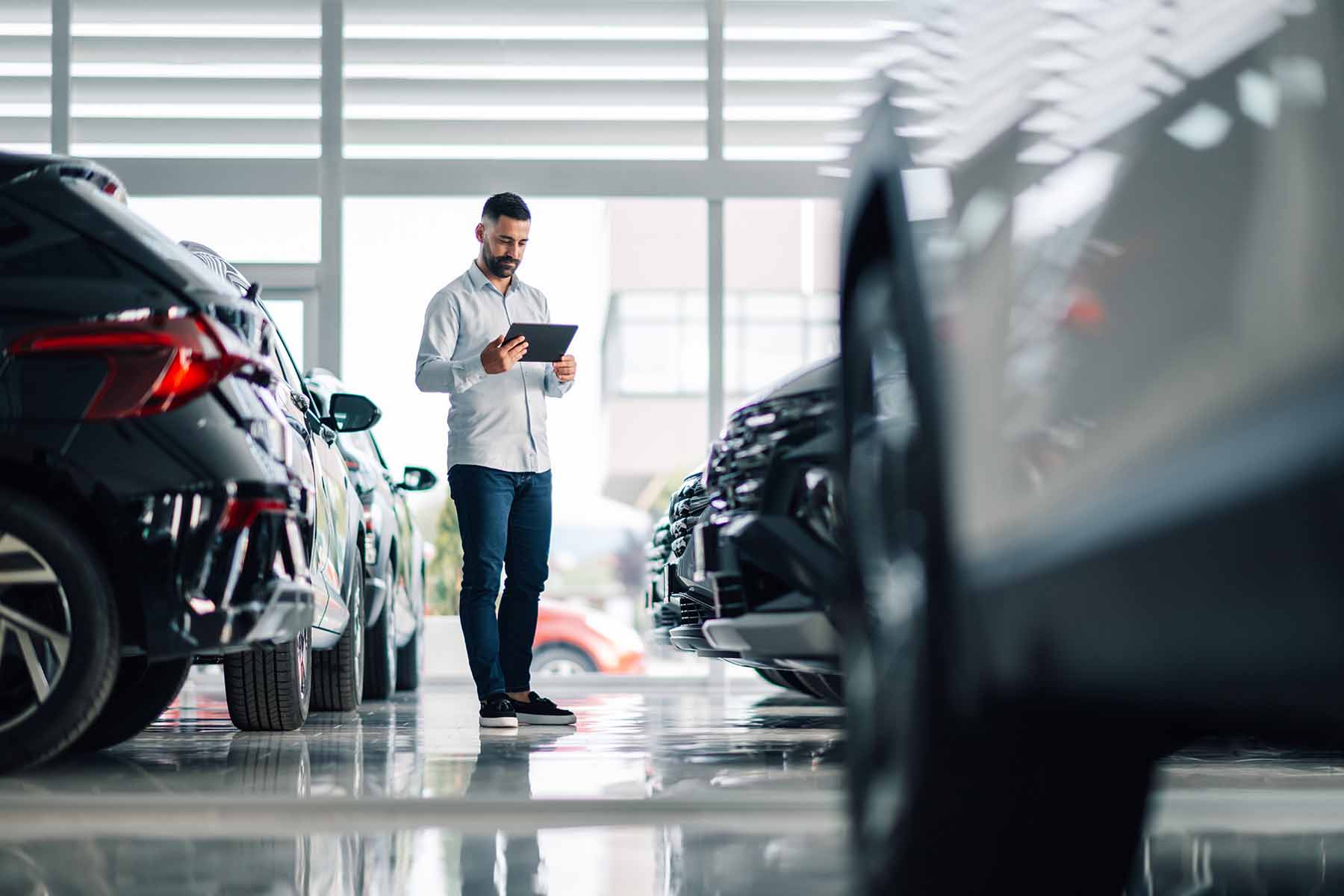Person using a tablet in a car showroom with vehicles parked on both sides.