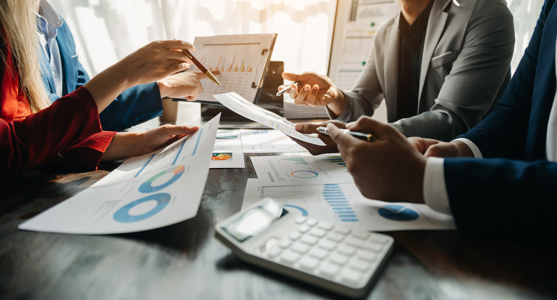 4 people at a table pointing to papers with graphs and charts on them