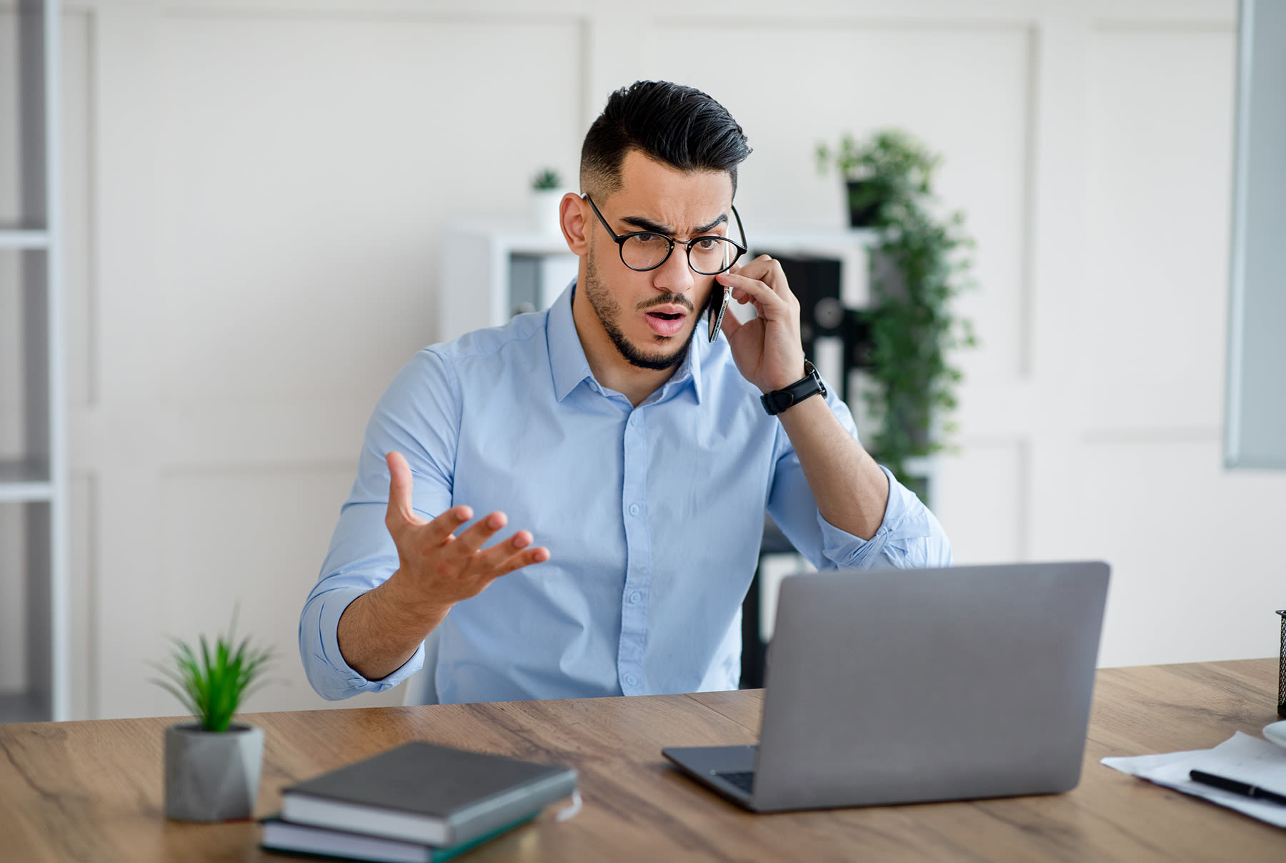 frustrated person talking on a phone and looking at a laptop
