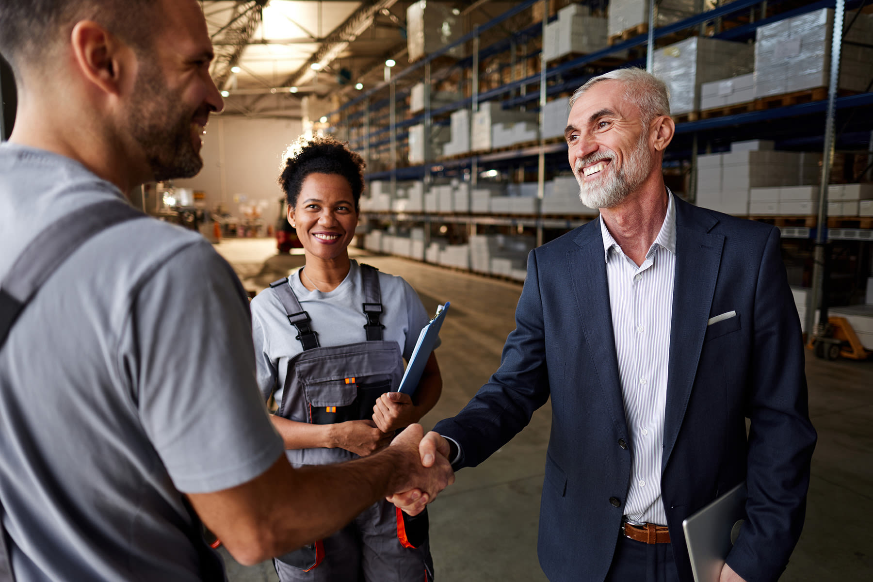 Three individuals smiling and shaking hands in a warehouse