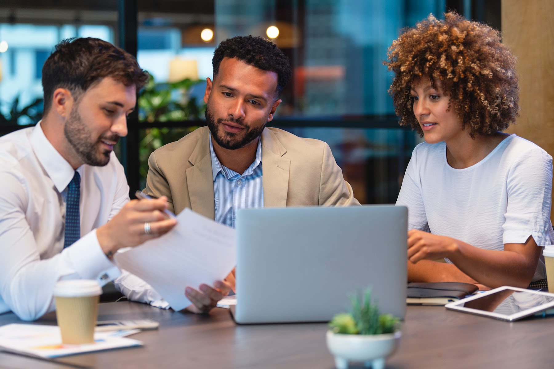 Three people are sitting at a table in an office setting, engaged in a discussion.