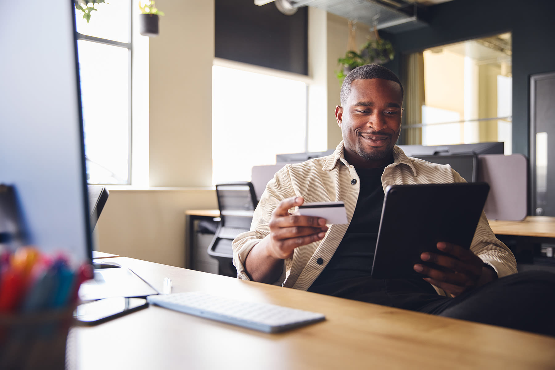 A person at a desk that is holding a credit card and looking at a tablet