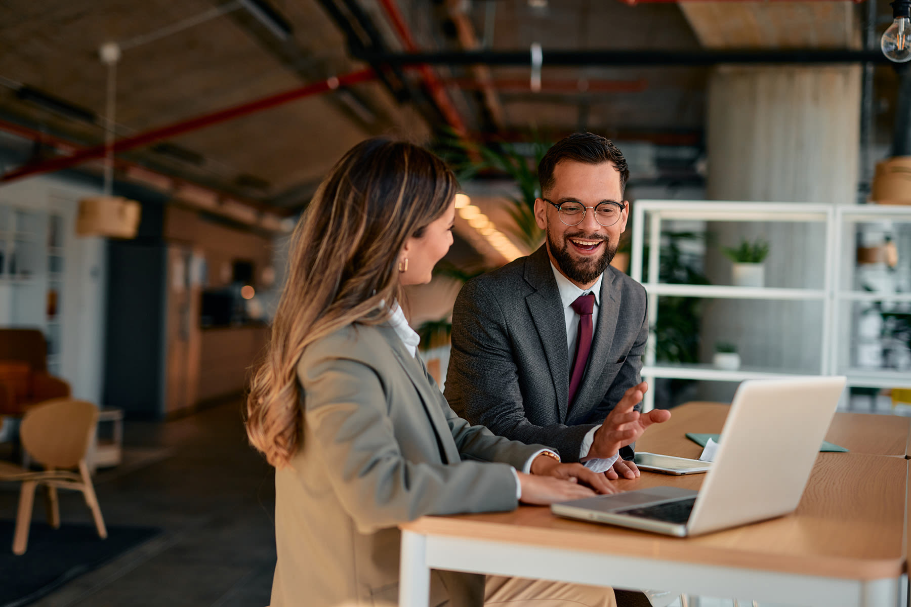Two business professionals conversing at a table and looking at a laptop in a rustic office
