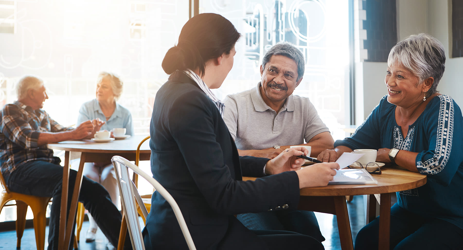 Four individuals seated around a table in a cafe, with their faces obscured by brown rectangles.