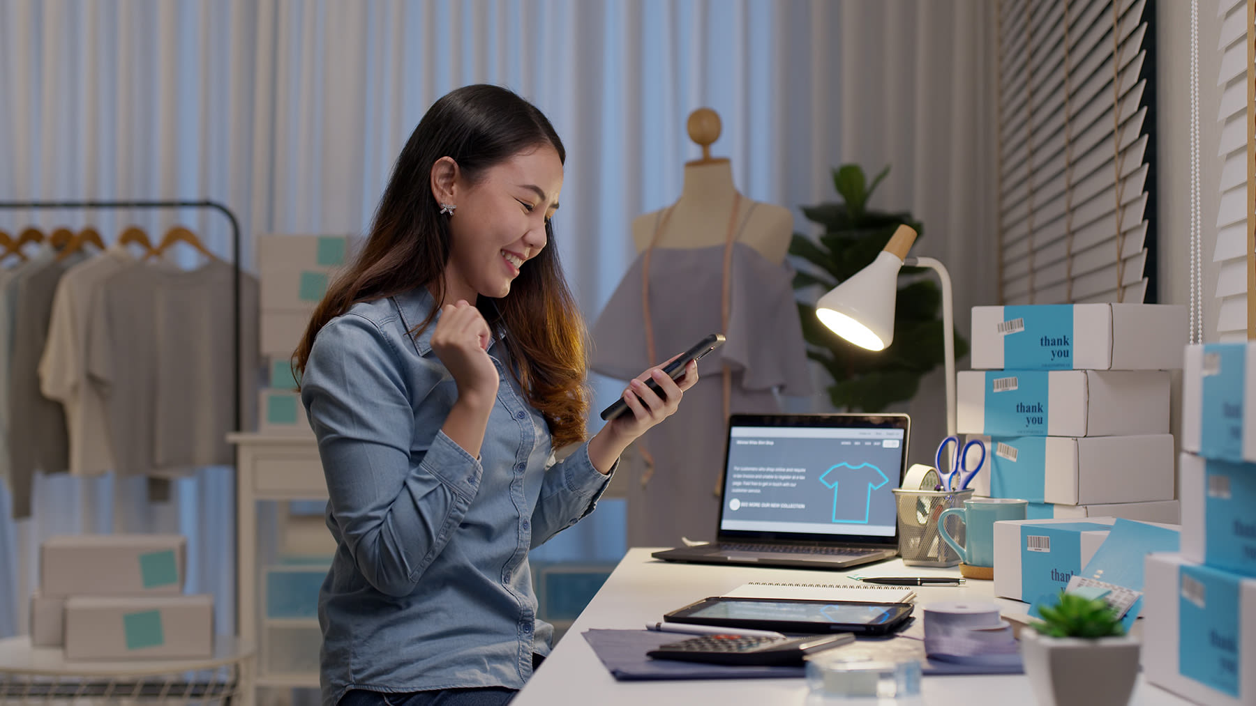 A lady sitting at a desk and excitedly looking at her phone.