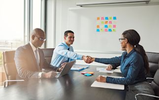 three people meeting around a table and two of them are shaking hands
