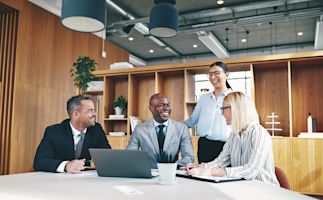 4 workers gathered around a table and are smiling and laughing