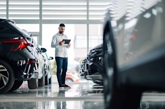 Person using a tablet in a car showroom with vehicles parked on both sides.