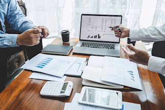 Two professionals analyzing data on a laptop and printed documents, in a bright workspace.