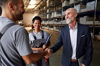 Three individuals smiling and shaking hands in a warehouse