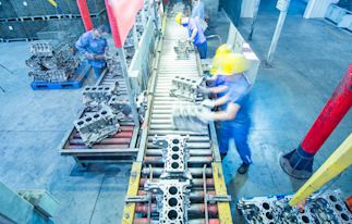 Manufacturing production line with industrial equipment and workers assembling engine components, representing a business supported by asset-based lending during ownership or operational transitions.
