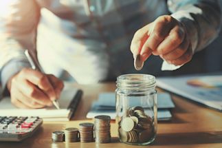 person putting a coin into a savings jar