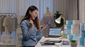 A lady sitting at a desk and excitedly looking at her phone.