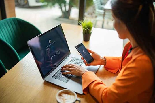 person looking at cell phone and typing on computer