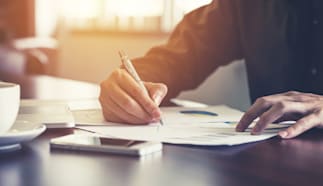 Close up of a person’s hand holding a pen writing on SBA loan application.