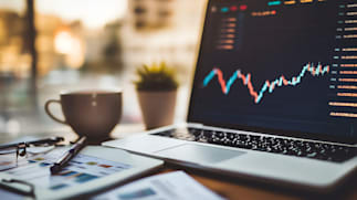 close up image of a laptop showing stock prices on a table with a blurred background behind it