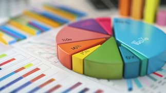 A colorful 3D pie chart with percentages on a desk, surrounded by various bar graphs and data sheets.