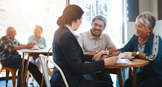 Four individuals seated around a table in a cafe, with their faces obscured by brown rectangles.